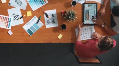 Proje yöneticisi renk paletleri seçerken tasarımcının tablete baktığı yukarıdan aşağıya hava görüntüsü. Profesyonel grafik tasarımının en üst görüntüsü ve logoya bakın. Yetenekli ekip grafikleri seçiyor. Sempozyum.