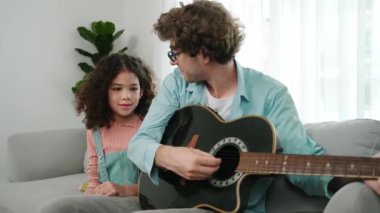 Beyaz bir baba, tatlı kızına koltukta otururken gitar çalmayı öğretiyor. Müzik öğrenirken babasına gitar çalarken bakan tatlı öğrenci kız. Aile eğlence konsepti. Pedagoji.