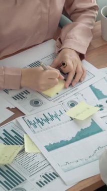 Ofis masasında çalışan iki hevesli genç iş kadını, veri tablosu raporlarıyla birlikte. Genç meslektaşlar istatistik veri kağıdı planları ve stratejisini tartışıyor ve analiz ediyorlar.