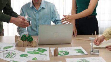 Yel değirmeni modeline ve ev şeklindeki bloğa danışmanlık yapan işadamları, Dünya Yöneticisi 'nin dizüstü bilgisayar üzerinde çalışmasını kurtarmak için yeşil enerji kullanımına referans olarak başvuruyorlar. Tanımlama.