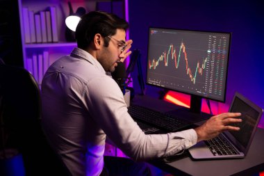 Akıllı tüccar işadamı, karanlık oda gecesinde neon ışıklı ofisteki arama pazarında yüksek kârla ekranda bilgisayar ve bilgisayar üzerinde dinamik borsa yatırımları üzerinde yoğunlaşıyor. Tahmin et..