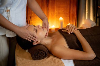 Beyaz kadın stres önleyici kafa masajı yapmaktan ve lüks otel veya otelde sıcak mum ışığında yüz güzelliği eğlencesi yapmaktan zevk alıyor. Sessiz.