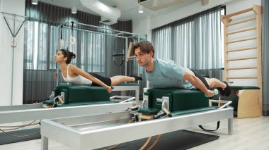 Erkek ve kadın spor salonunda vücut ve sırt kaslarını güçlendirmek için pilates sandalyesi üzerinde egzersiz yapıyorlar. Pilates partneri sırtının üst kısmını güçlendirmek için yenilikçi olmaya eğilimli. Alışkanlık.