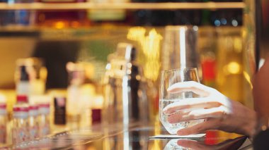 Yakından bir müşteri eli cin fizz ya da tonik ile Bokeh 'in sıcak gece kulübünün atmosferinde lüks bir bar manzarasında. Geceleri arkadaşlarla ya da barlarda ya da restoranlarda bir çiftle yaşam tarzı. Vinosity.