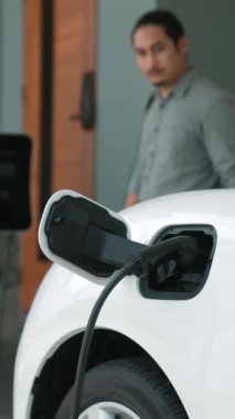 Adamın biri evinde elektrikli araç şarj aletinin fişini çekiyor. İlerici bir yaşam tarzında elektrikli araçların kullanımı, temiz ve sağlıklı bir çevreye katkıda bulunur..