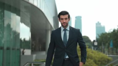 Profesyonel iş adamı hareket ediyor ve kameraya bakarken ayakta duruyor. Gülümseyen yönetici kameraya kendinden emin bir şekilde gülümsüyor. Mimari binada takım elbiseli yatırımcıların yakın çekimi. Sevinçli..