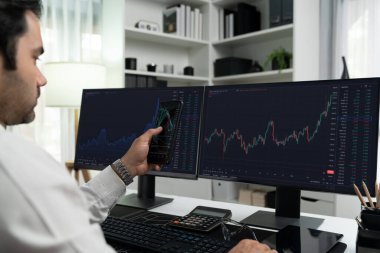 Akıllı telefondan akıllı telefon arayan tüccar işadamı, bilgisayardaki dinamik borsa yatırım ekranını analiz ediyor ve modern merkez ofisteki en kârlı finansal teknoloji pazarına yatırım yapıyor. Tahmin et..
