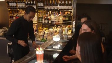 Güzel arkadaşlar lüks bir barda Paloma ve Margarita ile konuşup içerken barmen de güzel bir çiftle parti havasında kokteyl hazırlıyor. Vinosity.