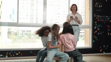 Çeşitli çocuklar sandalye kapmaca oynarken genç ve güzel öğretmenler müziği kapatıyor. Çok kültürlü öğrenciler yaratıcı aktivitelerde sandalyede koşup oturuyorlar. Müzik dersi. Etkinlik.