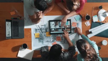 İnşaat mühendislerinin masa başında proje planıyla otururken tablet kullanarak ev yapısını dizayn etmelerine tepeden aşağı bir bakış açısı. Ekip planlama ve inşaat hakkındaki fikirlerin havadan görüşü. Sempozyum.