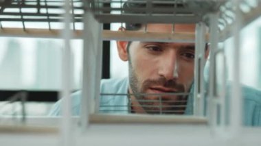 Ev modeli yapısını kendinden emin bir şekilde kontrol etmeye odaklanan beyaz yetenekli mimar mühendisinin yakın çekimi. Ev inşaatına bakan erkek işçi. Yaratıcı tasarım konsepti. İzleme