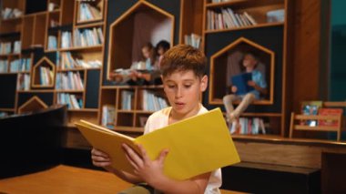 Bir grup zeki öğrenci kütüphanede otururken beyaz çocuk kitap okuyor. Çekici çocuk ders çalışıyor, çocuklar konuşurken romandan ya da kitaptan öğreniyor, eğitim hakkında sohbet ediyor. Etkinlik.