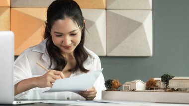 Güzel genç mimar mühendisinin portresi ev modelini ölçerken aynı zamanda dizüstü bilgisayar, proje planı ve masanın üzerine yerleştirilmiş taslağı da alıyor. İş tasarımı konsepti. Yönlendirici.