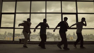 Yetenekli koreograf grubunun gökyüzü dövüşçüsüyle dans ederken çekilmiş siluet fotoğrafı, şehir manzarası arka planı. Genç hipster takımı dans gösterisi. Sepia filtresi. Gölge. Açık hava sporu 2024 hiphop..