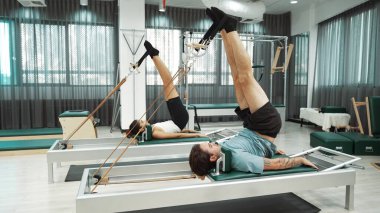 Müşteri, spor salonundaki yenilikçi bir makinede kayışla ters bacak kaldırma hareketi yapıyor. Çekirdek bağlantısını, dengesini ve esnekliğini geliştirmek için ters takla atan iki mutlu antrenör. Alışkanlık.