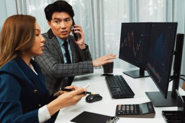 Gülümseyen Asyalı işadamı komisyoncu dinamik borsa veritabanını arıyor. Kadın iş ortağı, iç işyerindeki kar eden uygulama programını karşılaştıran ekranlara işaret ediyor. İnfobahn.