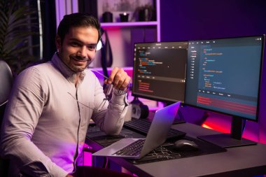 Gülümseyen akıllı bilişim geliştiricisi dizüstü bilgisayar üzerinde çalışırken kameraya bakıyor, neon ışıklı ofis odasında yazılım kodlama sistemi, uygulama programı güncellemesi yapıyor en son online web sitesi verileri. Tahmin et..