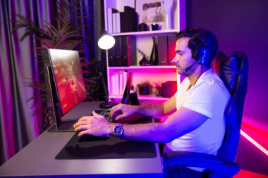 Kulaklık takan akıllı oyun flaması hafta sonu neon dijital siber ışıklandırma odasında son yaşam tarzı yarışmasında şampiyon olmak için bilgisayar ekranında araba yarışı oynamaktan zevk alır. Tahmin et..