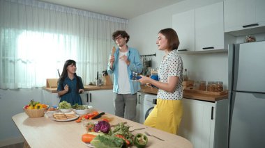 Beyaz yetenekli baba, anne ve Asyalı kız birlikte dans ederken kahvaltı hazırlıyorlar. Modern mutfakta sebze hazırlarken ukulele çalan yetenekli bir anne. Sağlıklı gıda konsepti. Pedagoji.