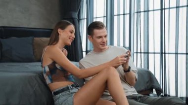 Genç çift, kredi kartıyla ödemek için internet üzerinden ödeme uygulaması ve dijital cüzdan kullanarak yatak odasında oturuyor. Mobil internet üzerinden alışveriş ve modern alımlar. Düzenle