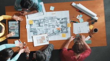 Toplantı odasındaki planlara bakan akıllı mühendisin yukarıdan görünüşü. Yetenekli mimar takımı konuşur ve tartışır. Proje planında planlarla toplantı masasını incelerken. Sempozyum.