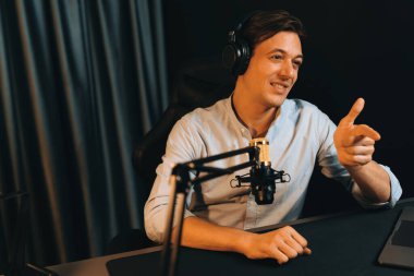 Sunucu kanalı akıllı yayıncı laptopta canlı sosyal medya uygulaması arıyor, kulaklık takıyor ve modern ofis stüdyosundaki mikrofonu kullanıyor. Bireysel.