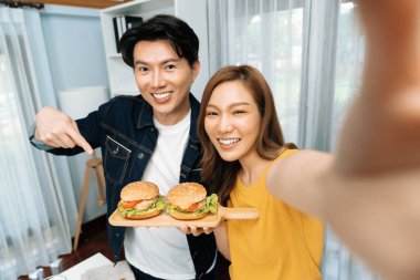 Gülümseyen sunucu şefler akıllı telefonlarıyla fotoğraf çekiyorlar. Özçekim yoluyla. Yemek programında çift hamburger tutuyorlar. İnfobahn.