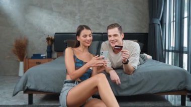 Genç çift, kredi kartıyla ödemek için internet üzerinden ödeme uygulaması ve dijital cüzdan kullanarak yatak odasında oturuyor. Mobil internet üzerinden alışveriş ve modern alımlar. Düzenle