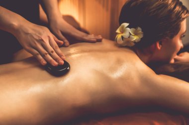 Sıcak mum ışığı olan lüks bir tatil köyündeki kaplıca salonunda sıcak taş masajı yapan mutlu çift, bazalt taşı masajının keyfini çıkarırken rahatlatıcı bir sıcaklıkla vücudun üzerinde süzülüyor. Sessiz.