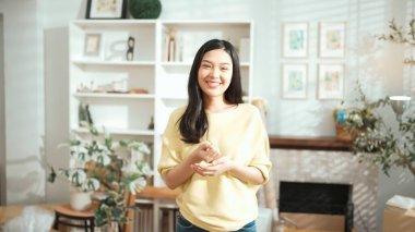 Genç girişimci ev ofisinde dikilirken kameraya bakıyor. Kendine güvenerek gülümserken kameraya özgüvenle bakan mutlu kadın satıcı. Küçük işletme ya da başlangıç konsepti. Myrmidon.