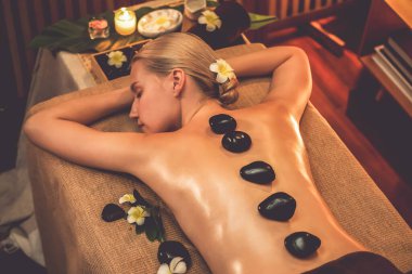 Lüks tatil köyündeki kaplıcalarda sıcak taş masajı, sıcak mum ışığı, spa bazalt taşı masajının keyfini çıkaran mutlu kadın müşteriler, rahatlatıcı bir sıcaklıkla vücudun üzerinde süzülüyorlar. Sessiz.