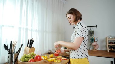 Enerjik anne, mutfak malzemeleri ile çevrili sebzeleri doğrarken modern mutfakta kahvaltı için salata yapıyor. Akıllı kadın temizlikçi yemek pişirir ve yemek hazırlar. Sağlıklı bir yaşam tarzı. Pedagoji.