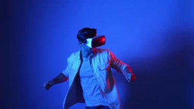 Sanal dünyada kılıç ve eskrim yaparken VR gözlük takan zeki bir oyuncu. Çekici erkek model, mavi arka planda dikilirken ve metaevrene erişirken aksiyon oyunu oynuyor. Aygıt.