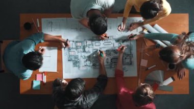 İnşaat mühendisi ekibinin renkli paletlerle toplantı masasında yazı yazması. Yönetici proje planlarına bakarken bir grup farklı insan plan yapıyor ve not alıyor. Sempozyum.