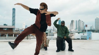 Bir grup profesyonel hip hop dansçısı çatıda break dans yapıyor. Becerikli koreograf serbest stil hareketini gösterirken, arkadaş da cesaretlendirir, alkışlar, alkışlar. Açık hava sporu 2024. Hiphop.