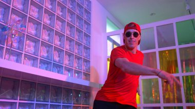 Komik break dansçı kameraya bakarken hiphop 'a doğru serbest adım atıyor. Çılgın mutlu hipster dans edip sokak dansı yaparken Led ışığında günlük kıyafet ve güneş gözlüğü takıyor. Mutluluk.