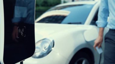 Bir adam kredi kartını, şarj istasyonundaki elektrikli aracının temiz ve sürdürülebilir enerjisini ödemek için kullanıyor. Yenilikçi adam şarj edilebilir aracına güç sağlamak için ödeme yapıyor..