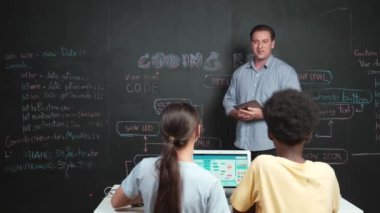 Kodlama programıyla ilgili öğrenci sorusuna beyaz öğretmen cevap veriyor. Beyaz kız, STEM teknoloji sınıfında dizüstü bilgisayar ekranı görüntülerken soru sormak, oy vermek, gönüllü olmak için elini kaldırdı. Öğretim