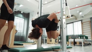 Profesyonel pilates eğitmeni, bir müşteriye jimnastik salonunda pilates yaparken rehberlik ediyor. Çekirdek dengesini ve omurilik hizasını iyileştirmek için çubuğa tutunan bir adam. Sağlıklı olmak. Alışkanlık.