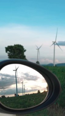 İlerleyen gelecek enerji altyapısı rüzgar türbini kavramı, rüzgar türbininin yeşil ve yenilenebilir enerjisiyle şarj edilen elektrik aracının yan aynasına yansıyor..