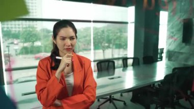 Profesyonel genç ve stresli iş kadını pazarlama sorunlarını çözmenin yollarını düşünürken aynı zamanda renkli yapışkan notlarla ve pazarlama fikriyle cam tahtada duruyor. Yönlendirici.