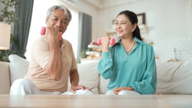 Mutlu yaşlı çift evde dambıllarıyla egzersiz yapıyor, kas gücü, eklem sağlığı ve sağlıklı yaşlanma için fiziksel sağlığa odaklanıyor. Emeklilik konsepti. Myrmidon.