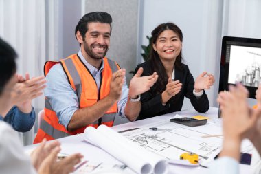 Çeşitli inşaat mühendisi ve müvekkil grupları, mimari proje üzerinde başarılı bir anlaşma sağlandıktan sonra heyecanlanıp alkışlanıyorlar, inşaat planını gözden geçiriyorlar ve toplantı masasında planlarını gözden geçiriyorlar.