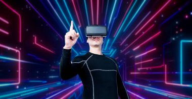 VR gözlüklü profesyonel erkek oyuncu parlayan neon ışıkla oyun oynuyor. Heyecanlı oyuncu artırılmış gerçeklik teknolojisi yeniliklerini kullanarak metaevrene bağlanmayı seviyor. Yaratıcılık.