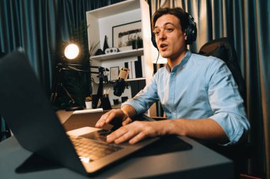 Sunucu kanalı akıllı yayıncı laptopta canlı sosyal medya uygulaması arıyor, kulaklık takıyor ve modern ofis stüdyosundaki mikrofonu kullanıyor. Bireysel.