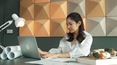 Modern ofiste proje planı, dizüstü bilgisayarı ve mimari modeli olan dizüstü bilgisayar analiz binası yapısını kullanan akıllı bir iç mimar. Asyalı proje yöneticisi bina tasarımını ölçüyor. Yönlendirici.