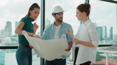 Profesyonel mimar mühendis ekibi konuşuyor, paylaşıyor, tasarım hakkında beyin fırtınası yapıyor. Yönetici planı dinlerken genç mimar plan yapıyor. İzleme