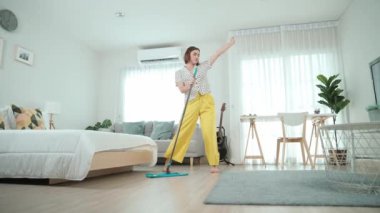 Modern apartman dairesinde dans ederken yerleri paspaslayan beyaz bir hizmetçi. Mutlu enerjik anne ya da temizlikçi müzik eşliğinde oturma odasını temizlemekten zevk alır. Yaşam tarzı. Pedagoji.