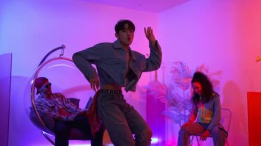 Çok kültürlü bir arkadaş kürsüde otururken Asyalı yetenekli bir dansçı modern müziğe geçiyor. Profesyonel dansçı, hipster takımı tezahürat yaparken ve desteklerken enerjik adımlar atıyor. Mutluluk.