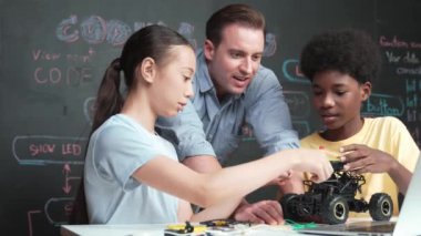 Kafkas öğretmeni dizüstü bilgisayarı işaret ederken araba modelleme sistemini kara tahtada kodlama veya programlama koduyla açıklıyor. Robot inşaatını öğrenen çeşitli öğrencileriniz kutlu olsun. Öğretim